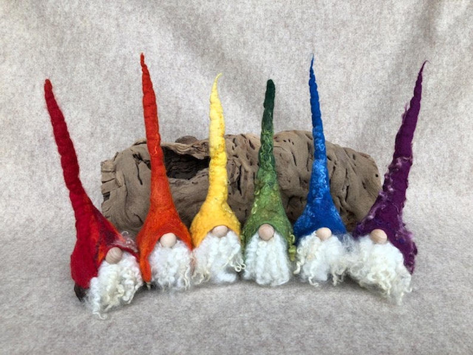 Six Christmas gnomes in a line next to each other each of them has a hat in one colour of the rainbow