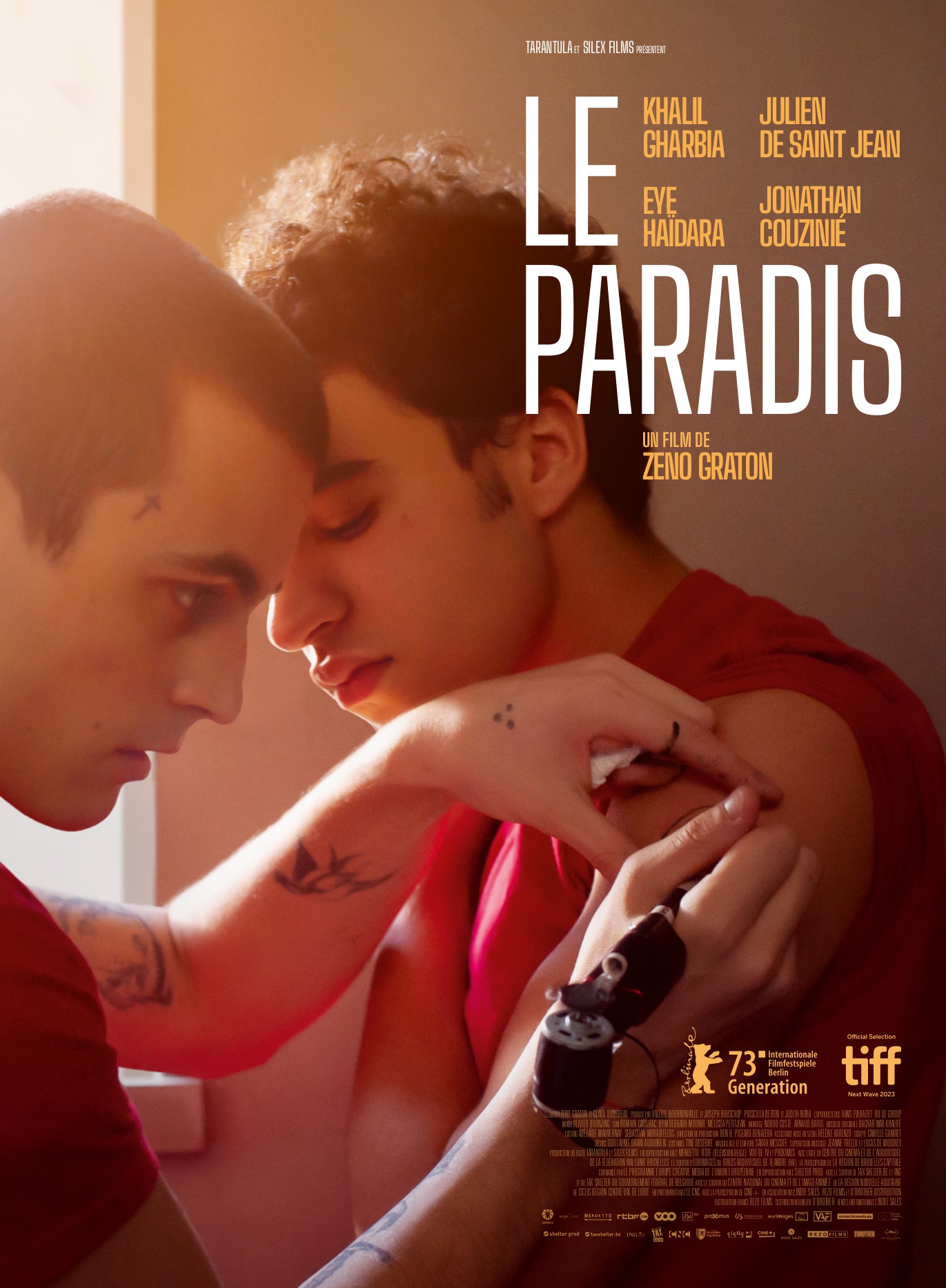 Filmposter van Le Paradis met de twee hoofdrolspelers. De jongens staan dicht bij elkaar. De een tatoeert de arm van de ander.