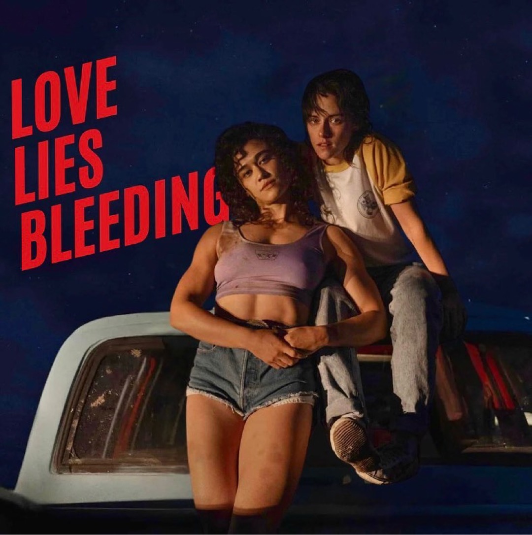 Twee hoofdrolspelers van Love Lies Bleeding poseren bij hun pick-up truck. Het is donker. Er staat een lamp die hen uitlicht.